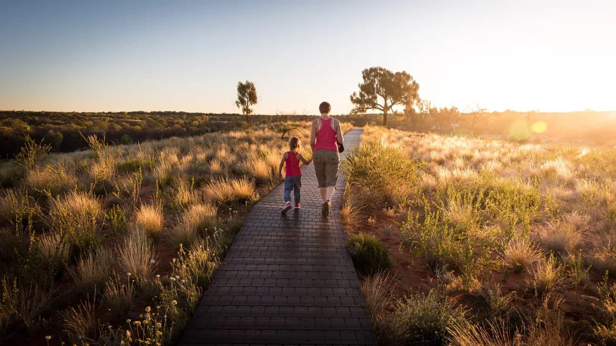 An adult and child walking together along a sunlit path